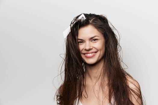 A joyful young woman with wet hair smiles brightly against a clean white background Her casual look conveys a sense of natural beauty and confidence, capturing an uplifting, fresh emotion in the photo