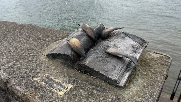 Tegernsee, Germany - March 30, 2025: Open book sculpture with fish, situated by the water of Lake Tegernsee, represents the connection between knowledge and nature