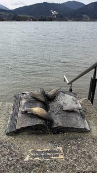 Tegernsee, Germany - March 30, 2025: Open book sculpture near the Bavarian lake features fish, set against a backdrop of mountains and natural beauty. Perfect for travel blogs.