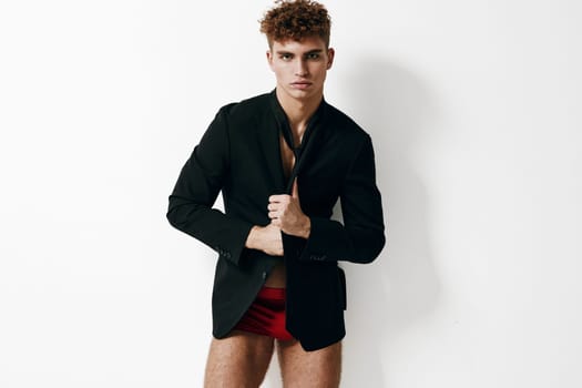 Fashion-forward young adult presenting a trendy look with a black blazer and red shorts, exuding confidence and style in a minimalistic setting.