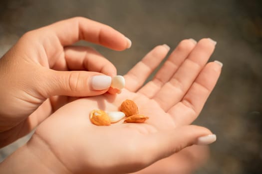 A person is holding a handful of nuts in their hand. The nuts are of different sizes and shapes, and they appear to be almonds. The person seems to be enjoying the nuts and is likely to eat them soon