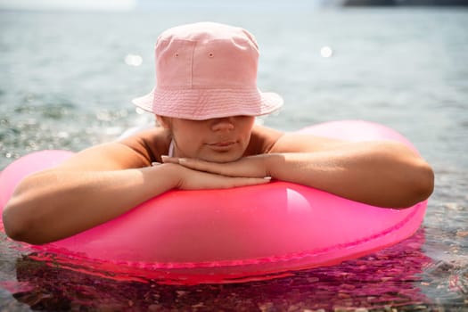 A woman is laying on a pink inflatable raft in the ocean. The scene is peaceful and relaxing, with the woman enjoying the water and the sun
