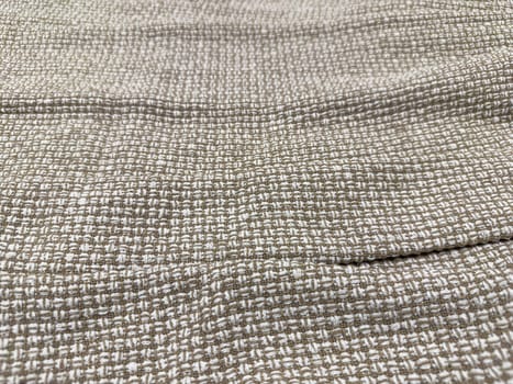 A close-up view of a woven fabric featuring a subtle pattern in soft beige and cream. The material has a textured surface, ideal for crafting and upholstery at home.