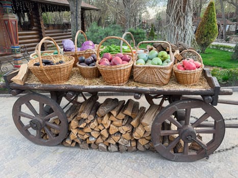 Baskets filled with various fruits like apples, plums, and peaches rest on a wooden cart. Surrounding greenery enhances the tranquil atmosphere of this charming outdoor scene.