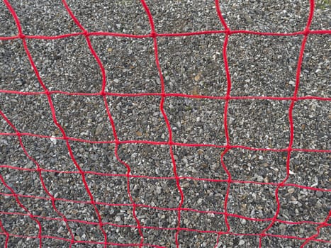 A red mesh fence surrounds a construction site, securing gravel and preventing access. The vibrant color contrasts with the gray gravel, creating a noticeable barrier.
