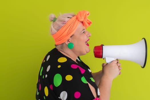 Confident woman in a colorful polka dot outfit and retro headwrap yelling into a megaphone, expressing strong emotion and attitude against a green background.