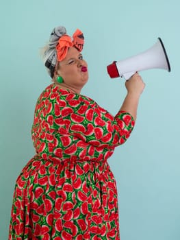 Confident woman in a colorful polka dot outfit and retro headwrap yelling into a megaphone, expressing strong emotion and attitude against a blue background.