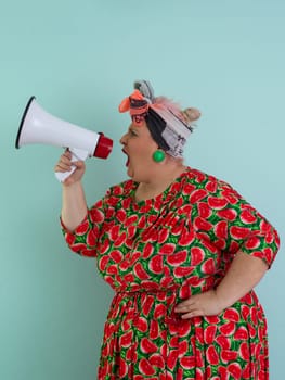 Confident woman in a colorful polka dot outfit and retro headwrap yelling into a megaphone, expressing strong emotion and attitude against a blue background.