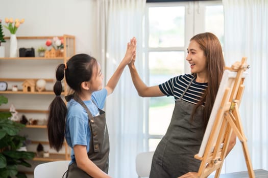 A proud mother and daughter high-fiving each other during a fun art session, celebrating creativity and teamwork in a cozy setting.
