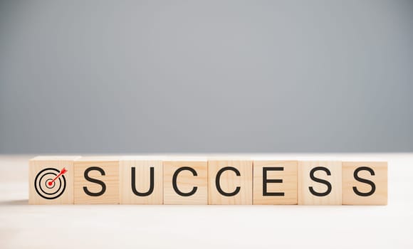 Wooden cube placed over the word success on a wood table, highlighting the target success concept. Captured on a grey background with ample copy space.