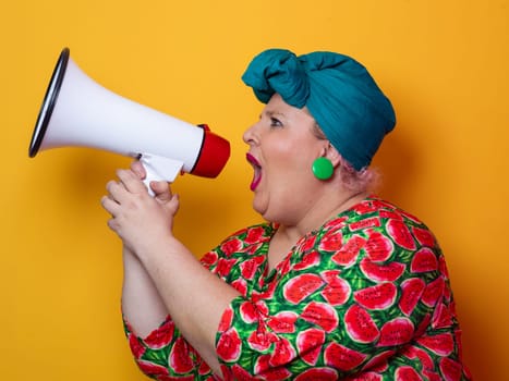 Confident woman in a colorful polka dot outfit and retro headwrap yelling into a megaphone, expressing strong emotion and attitude against a yellow background.