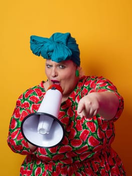 Confident woman in a colorful polka dot outfit and retro headwrap yelling into a megaphone, expressing strong emotion and attitude against a yellow background.