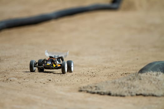 A toy car is driving on a sandy surface. The car is small and he is a remote control car. The image has a sense of playfulness and fun, as the toy car is moving around on the sand