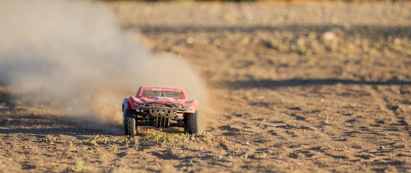 A red toy car is driving through a dusty field. The car is covered in dirt and the field is covered in dust