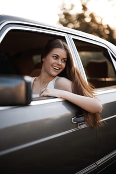 A cheerful young woman with long hair, leaning out of a car window, radiating happiness and excitement. Perfect for themes of travel, adventure, and summer vibes.