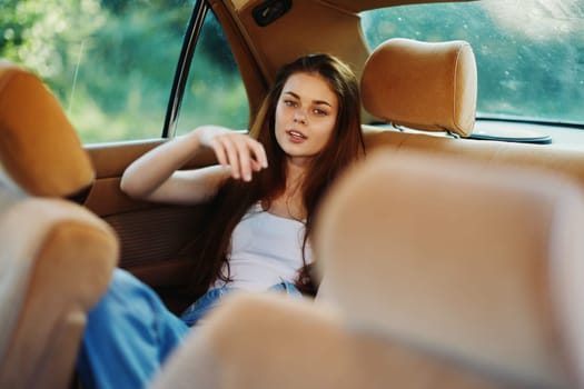 A young woman with long hair is lounging in the back seat of a vintage car, conveying a relaxed and carefree vibe amidst a beautiful green backdrop, perfect for moods of summer and freedom.