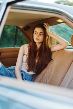 A young woman with long brown hair in a vintage car, dressed casually, portrays a thoughtful expression, embodying a relaxed summer atmosphere.