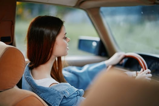 A young woman in a denim jacket drives a car, embodying a sense of freedom and contemplation, surrounded by a natural backdrop, perfect for seasonal lifestyle themes.