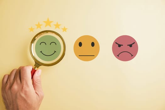 Magnifying glass held by hand selects happy smiley face icon among emotions. Good feedback rating, positive customer review. Experience, satisfaction survey, mental health concept. satisfaction.