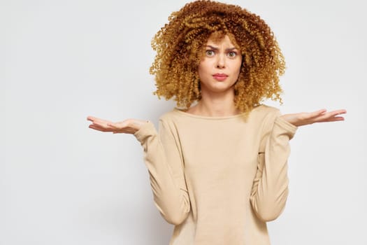 A young woman with voluminous, curly hair is standing against a plain white background, showcasing a look of confusion Her open hands express uncertainty, making this image suitable for themes relat