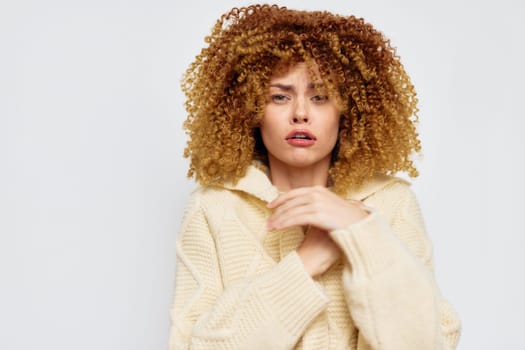 A fashionably dressed young woman with big curly hair in a cream colored sweater, presenting an contemplative mood The soft white background accentuates her beauty and the texture of her hair