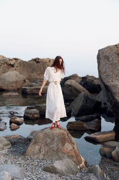 Serene white dress woman with red shoes standing on rock near water's edge