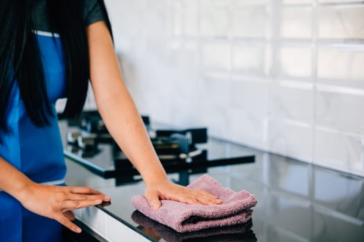 A cheerful housewife smiles while cleaning her kitchen table with a rag and detergent, ensuring safety and cleanliness. Illustrating routine household chores for a hygienic home.