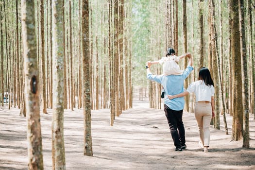 Family father carrying young girl shoulders while walking in forest with mother, Happy Asian family with adorable children in weekend, shoulder carry and happy family kid, dad and mom enjoy together