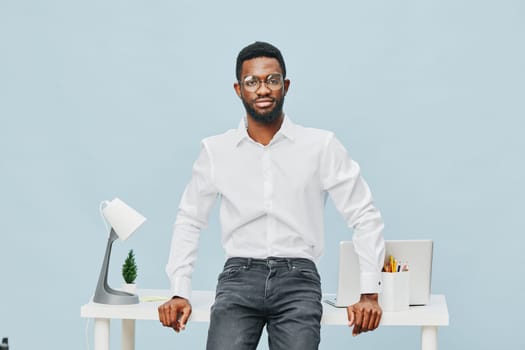 Happy young man with glasses and well-groomed appearance in casual white shirt standing at a clean desk with office supplies and a laptop, ready for work or a meeting. Concept: professional success and confidence.