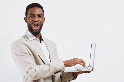 Confident smiling man with dark skin, short curly hair, dressed in a beige blazer and white shirt, holding a laptop and looking friendly, isolated on a plain white background, studio shot, conveying tech and professional success.