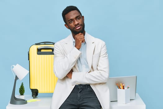 Stylish man in casual business outfit poses with laptop and suitcase in bright studio setting, deep in thought, illustrating readiness for work trip or business travel. Concept: professional journey and travel preparation.