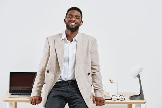 Smiling man in smart casual attire standing in a bright modern office with minimalistic decor and a laptop on the desk, creating a professional and approachable atmosphere. Concept: workplace positivity.