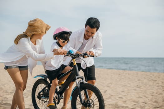Happy family moments on summer road trip, Parents teach their children to ride bicycles on sandy beach near sea. Smiles safety helmets and carefree spirit of childhood fill this cheerful scene.