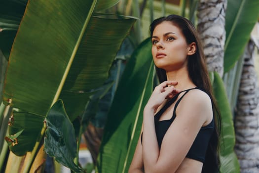 Confident woman in black bra top posing with hands on hips in front of tropical palm trees