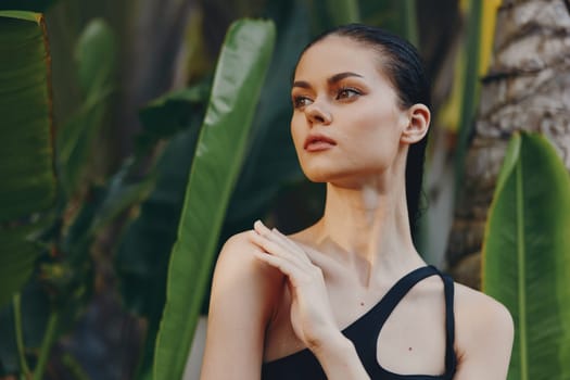 Woman in black tank top standing confidently in front of tropical palm tree with hands on hips