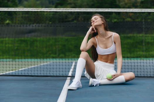 Relaxed athletic model in white sportswear sitting on tennis court, exuding happiness and confidence, perfect for themes of fitness, sports, and healthy lifestyle