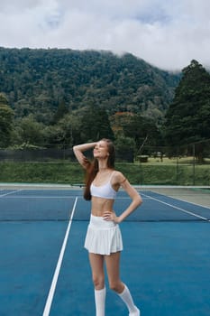 Joyful young woman in a white tennis outfit enjoying her time on the court, embodying a healthy lifestyle and athletic spirit in a vibrant outdoor setting