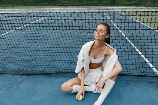 A young athletic woman sits on a blue tennis court, wearing a sporty outfit and smiling after practice The image conveys joy, fitness, and a healthy lifestyle with a vibrant and energetic atmosphere
