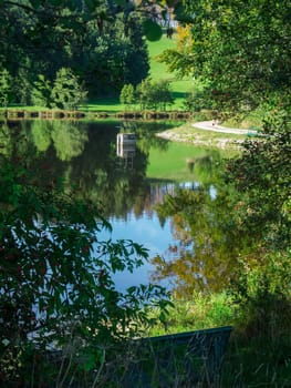 View of the idyllically situated Neuweiher with water level measuring shaft in Ostallgäu / Bavaria with trees in the foreground in summer 2023.