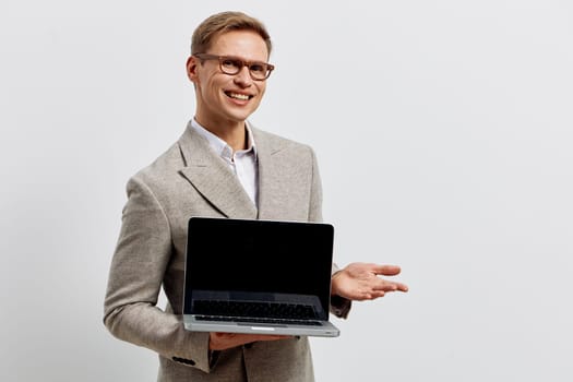 Cheerful man in smart attire presenting laptop with blank screen for business or technology purpose against plain white backdrop; professional, modern, confident concept