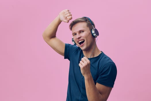 Happy young man with headphones on vibrant pink background, expressing fun and energy through a fist pump, cheerful mood, casual navy T-shirt, celebration, joyful lifestyle, studio shot. Concept: music enjoyment