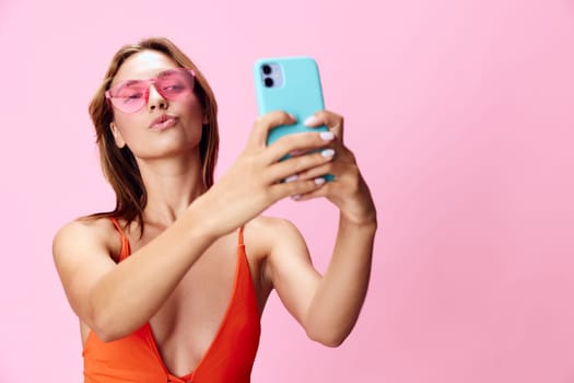 Trendy female posing in swimsuit, capturing a selfie using smartphone against vibrant pink backdrop