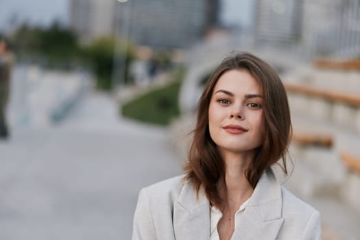 confident woman in light gray blazer outdoors smiling calmly with urban blurred background in autumn casual fashion style concept