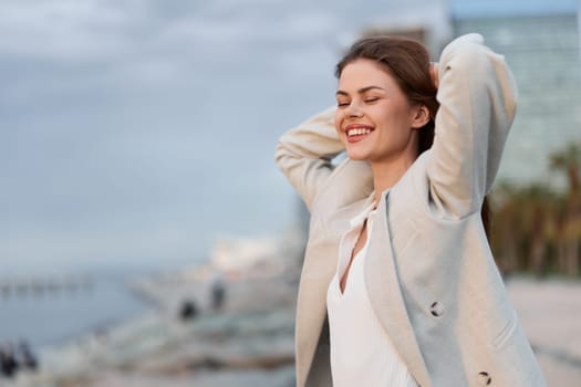 Joyful woman in elegant business clothing enjoying a moment by the seaside, showcasing confidence and positivity in a serene environment with a soft color palette.