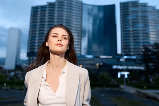 A confident businesswoman stands in an urban environment, wearing elegant attire that highlights her professionalism. The cityscape in twilight creates an inspiring backdrop. This image reflects ambition, empowerment, and success.