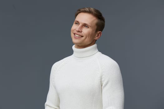 Portrait of a smiling man dressed in a white turtleneck sweater against a plain gray backdrop, showcasing a cheerful and relaxed demeanor, suitable for fashion, lifestyle, and portrait concepts.