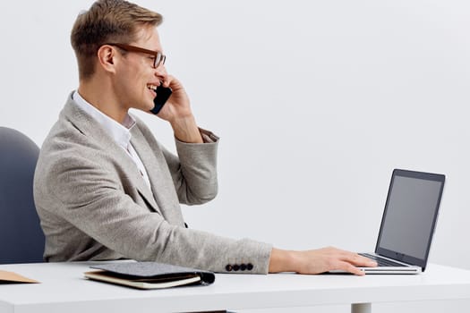 smiling man working with laptop and talking on mobile phone in modern office environment focused on smart home technology and digital nomad lifestyle with casual gray blazer and eyeglasses. Concept: smart home automation