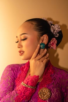 Asian woman in a pink dress trying to wear a green earring in her ears inside the studio
