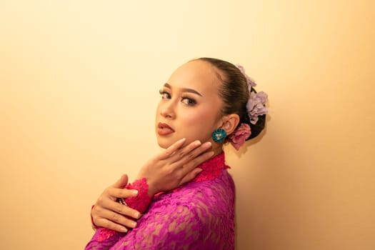 Asian woman in a pink dress trying to wear a green earring in her ears inside the studio