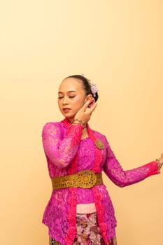 Asian woman in a pink dress trying to wear a green earring in her ears inside the studio